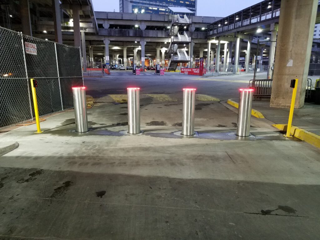 Stainless bollards with glowing red LED lighting at a nighttime entry point.