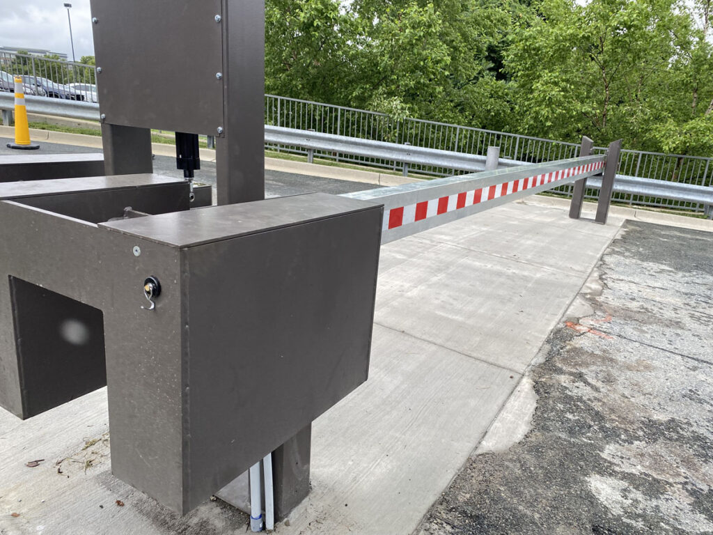 Automated red-and-white barrier arm extended across a concrete roadway.