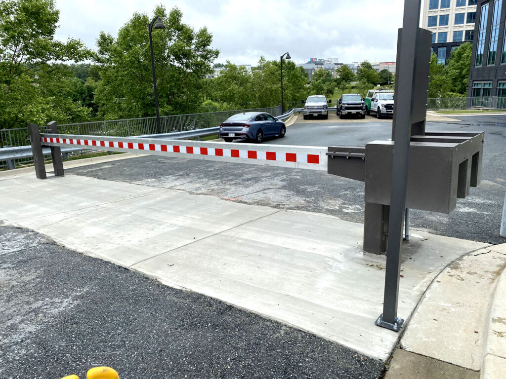 Automated barrier arm spanning a wide driveway leading to a parking area.