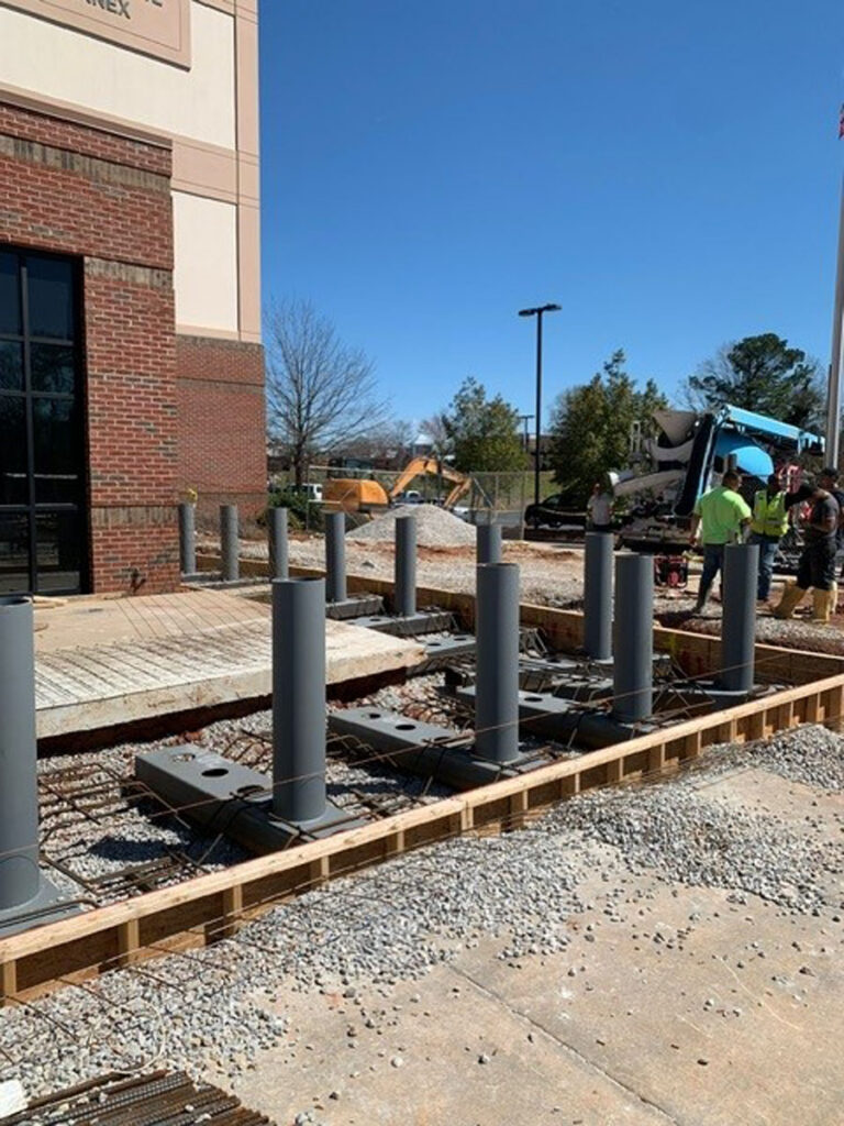 Construction crew installing bollard foundations outside a brick commercial building.