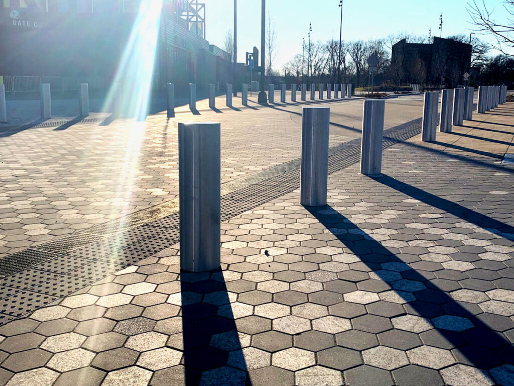 A long row of bollards lining a wide public walkway with patterned pavers.